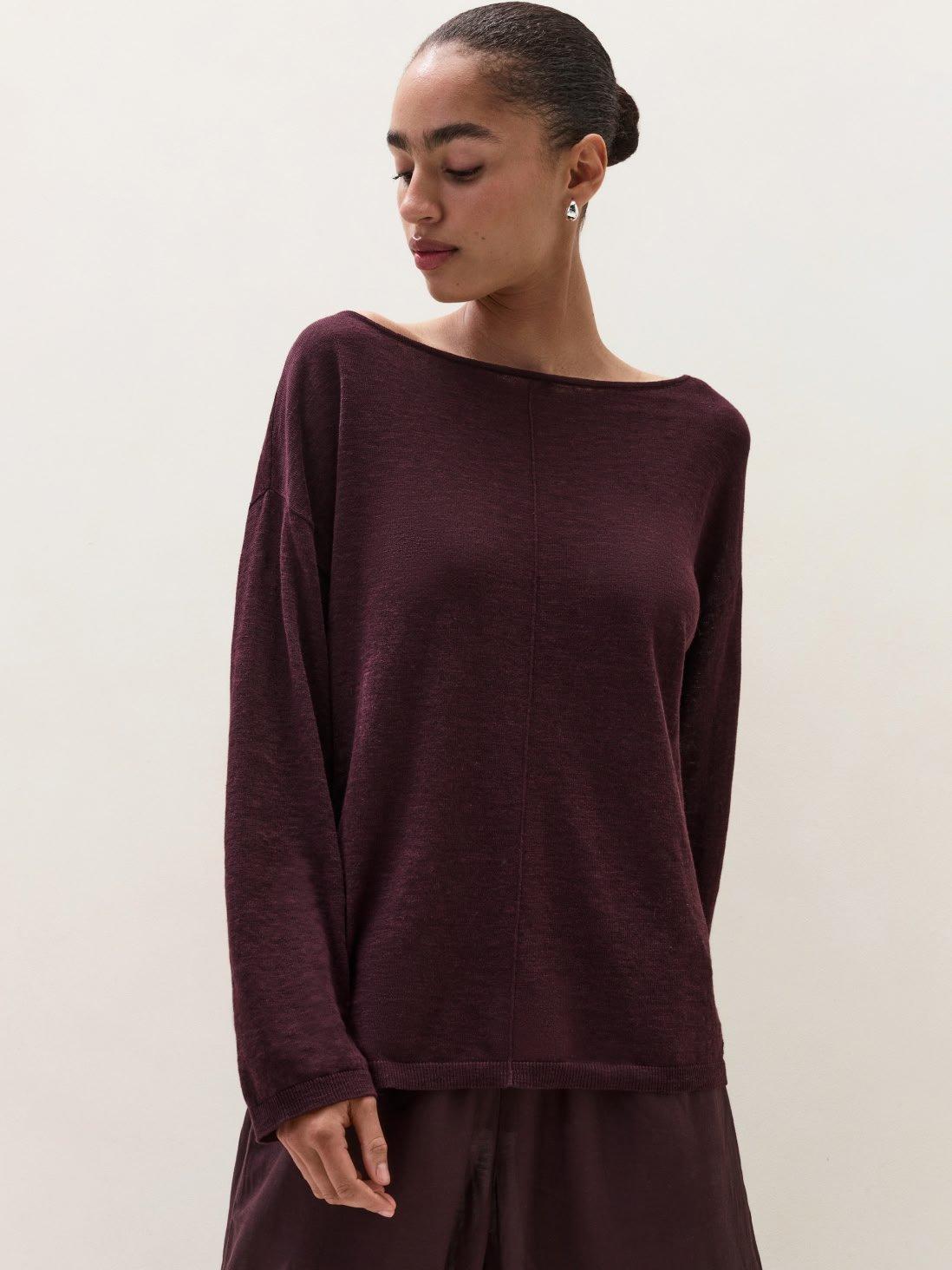 a woman in a maroon sweater and pants standing against a wall