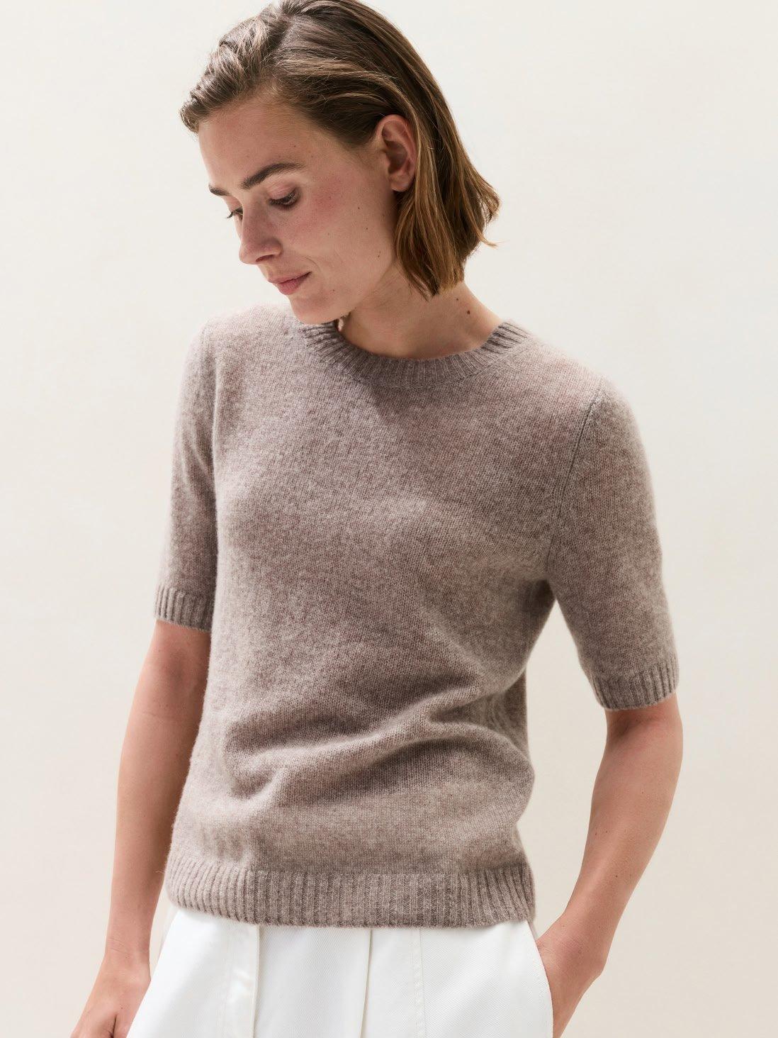 a woman in a grey sweater and white pants standing
