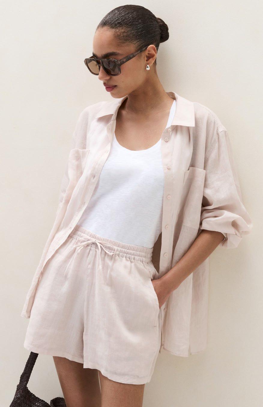a woman in a white shirt and shorts leaning against a wall
