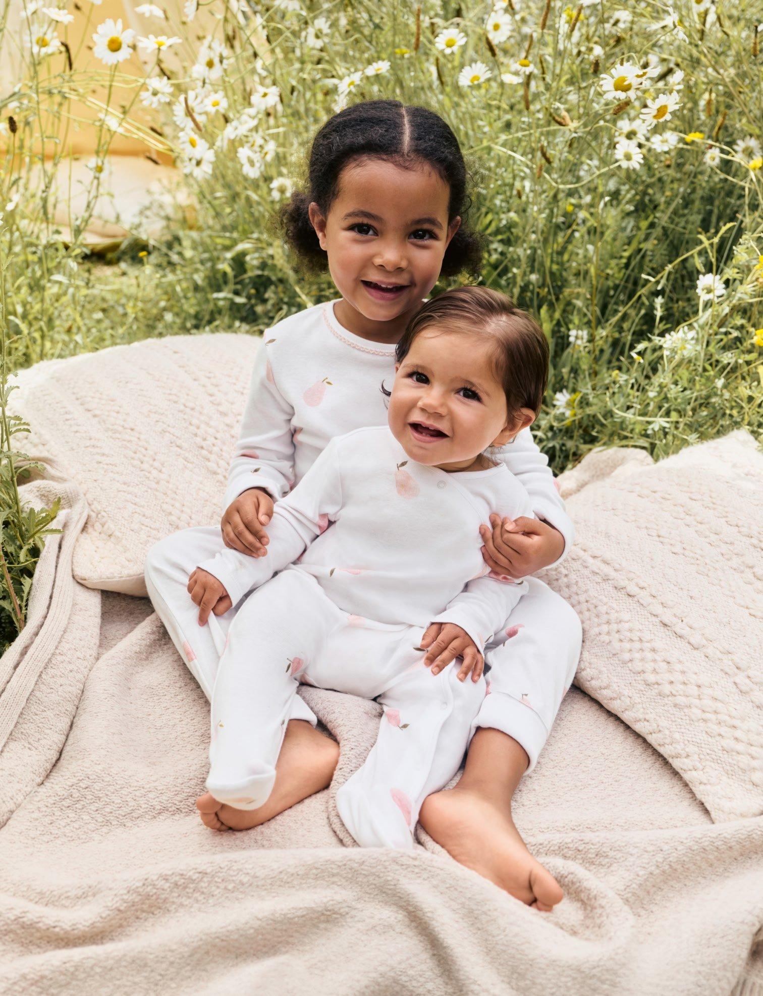 a baby in white pajamas standing next to a stuffed animal