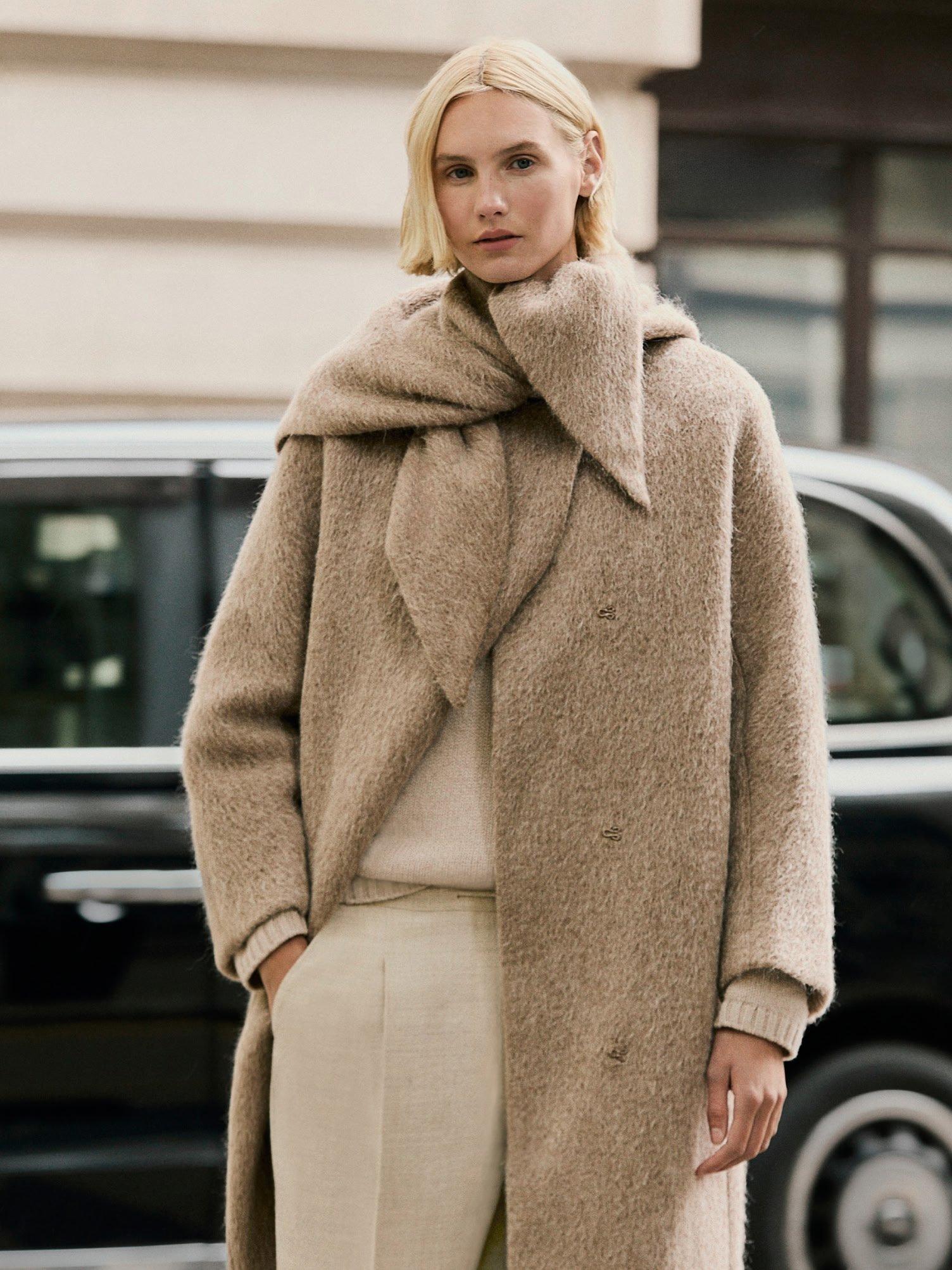 a woman in a beige coat and pants standing on the street
