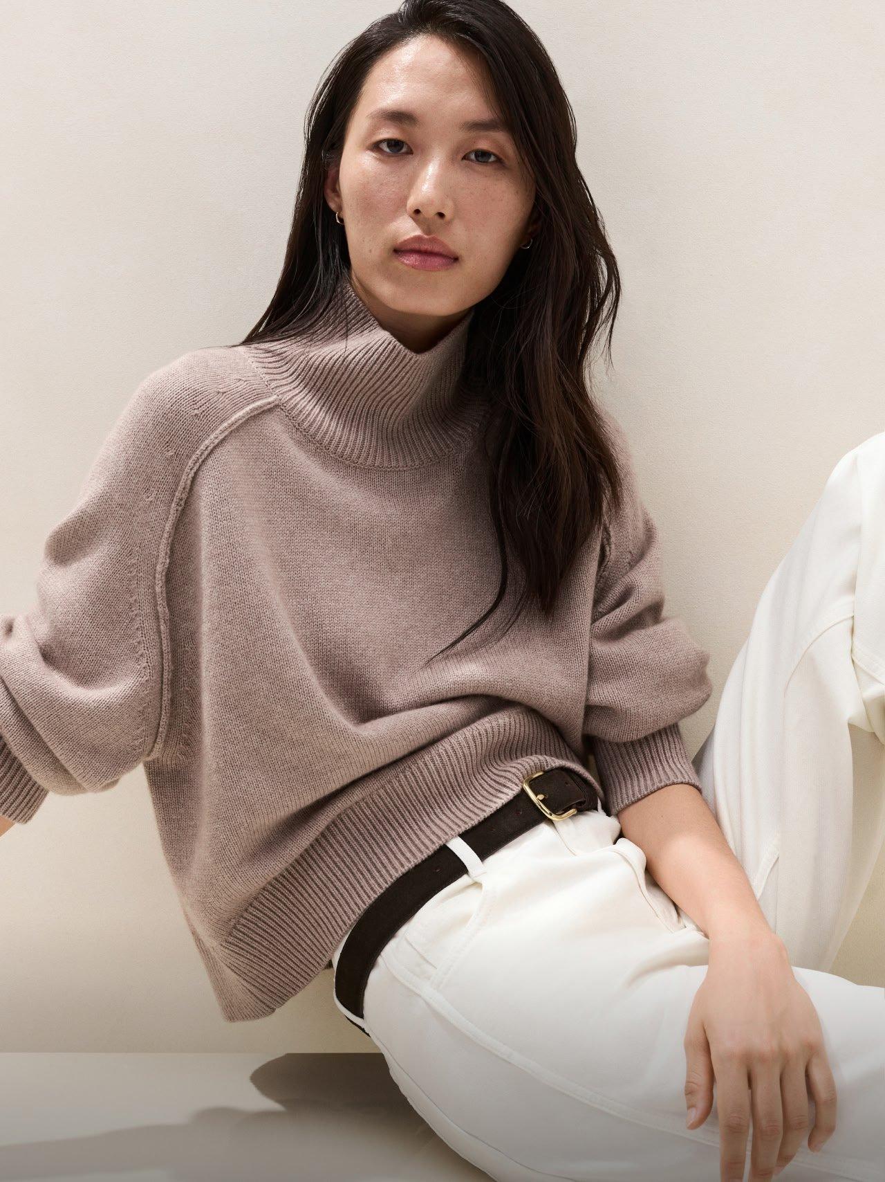 a woman in a turtle neck sweater and white pants sitting on a chair