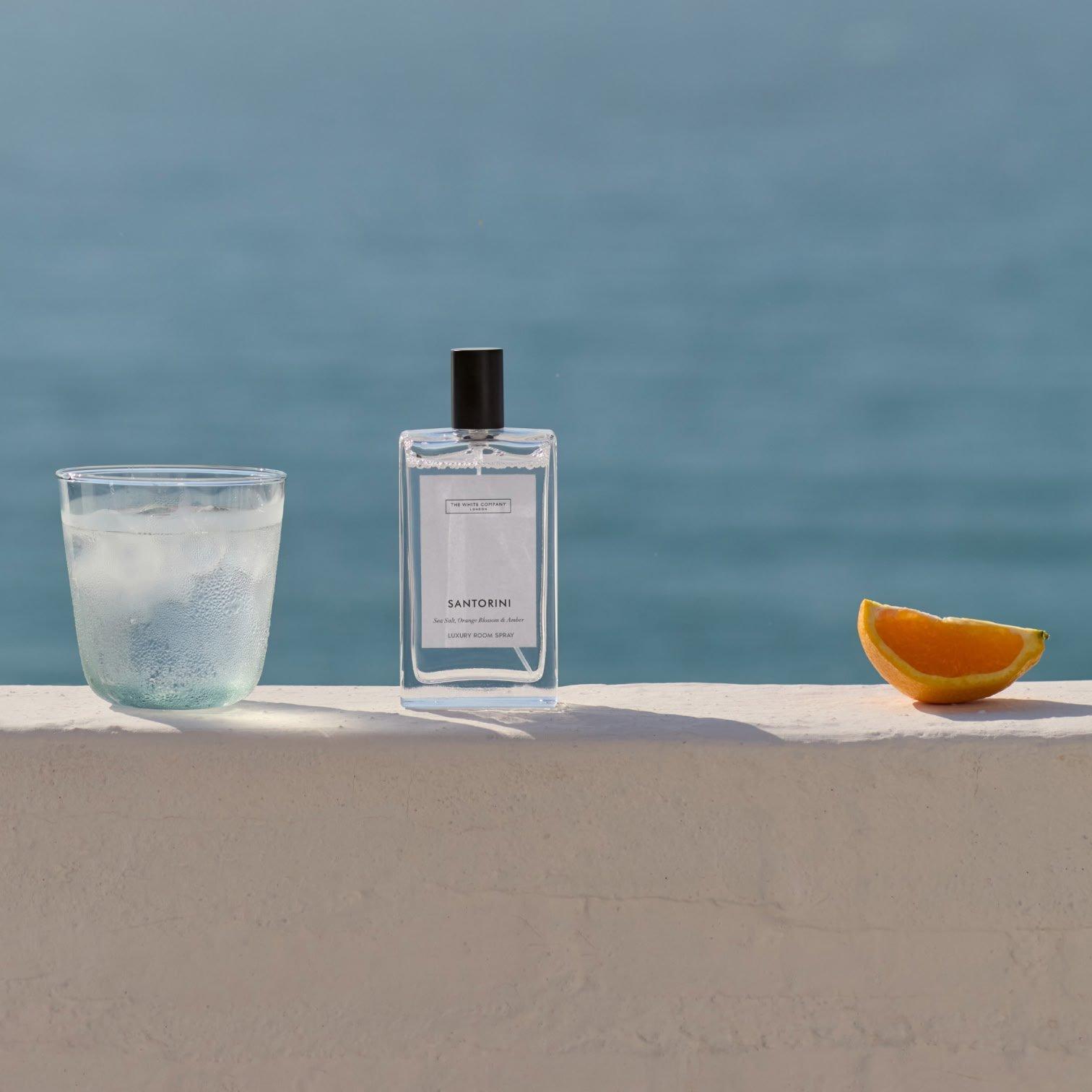 a glass of a bottle of perfume and an orange on a ledge