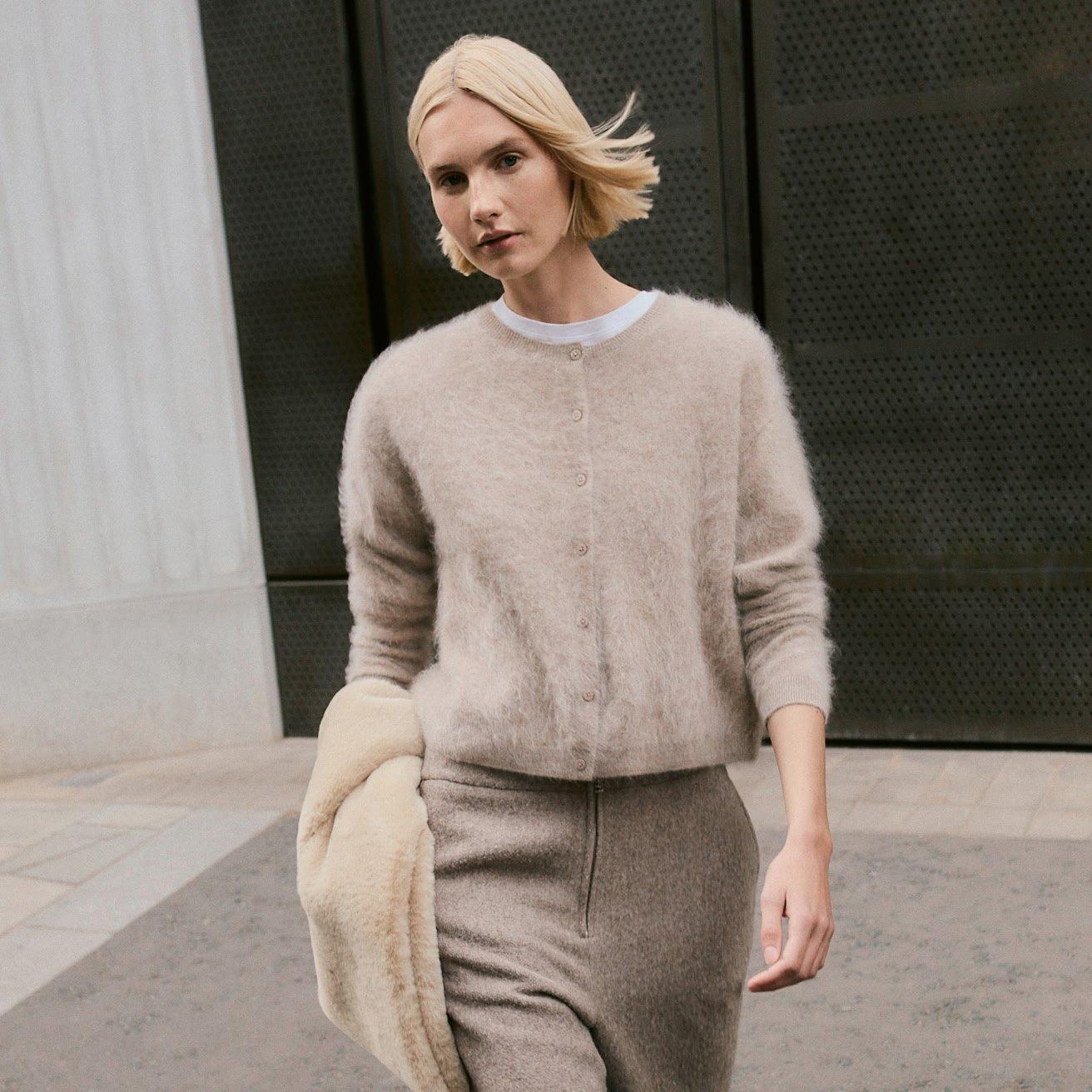 a woman in a beige sweater and skirt walking down the street
