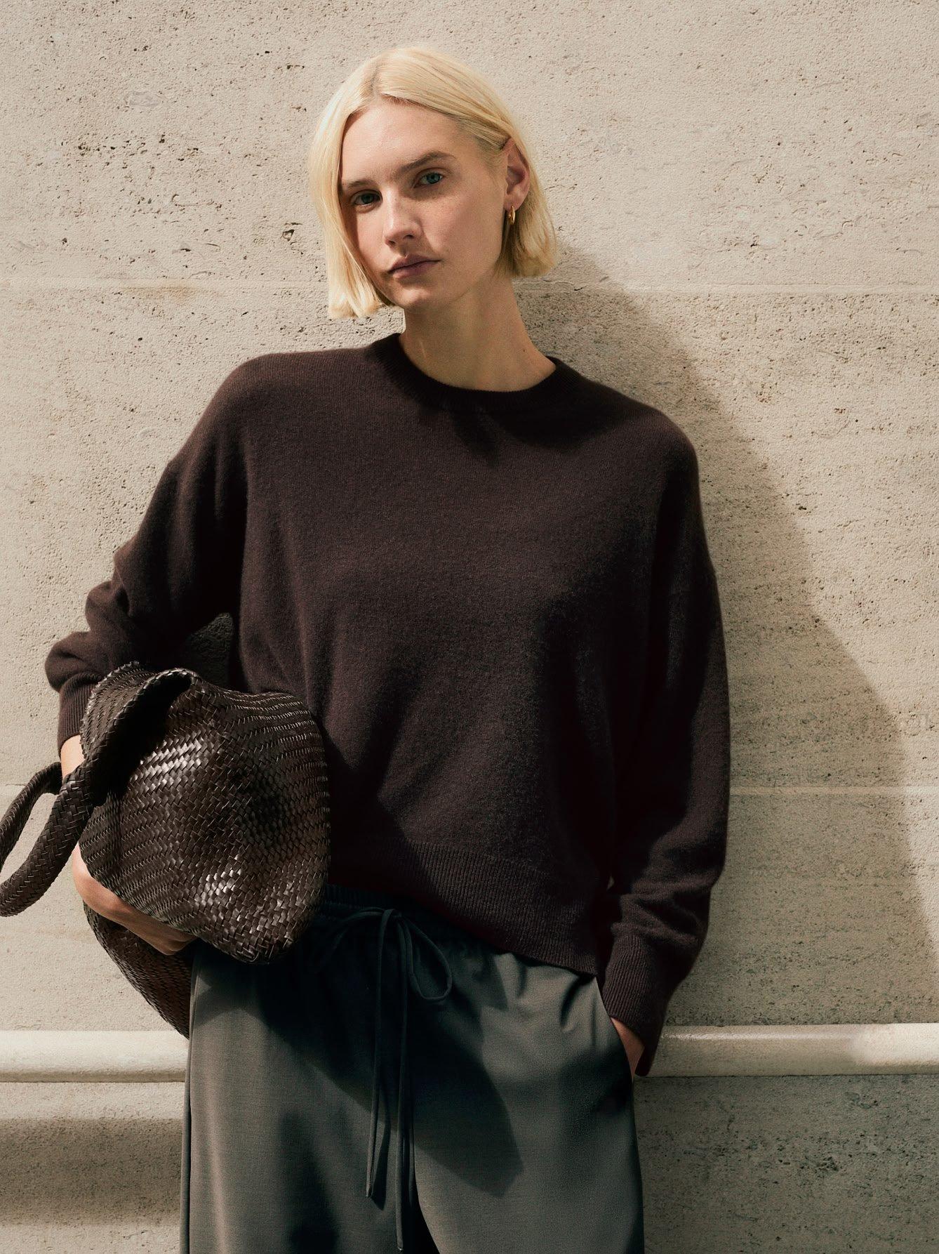 a woman in a sweater and pants leaning against a wall
