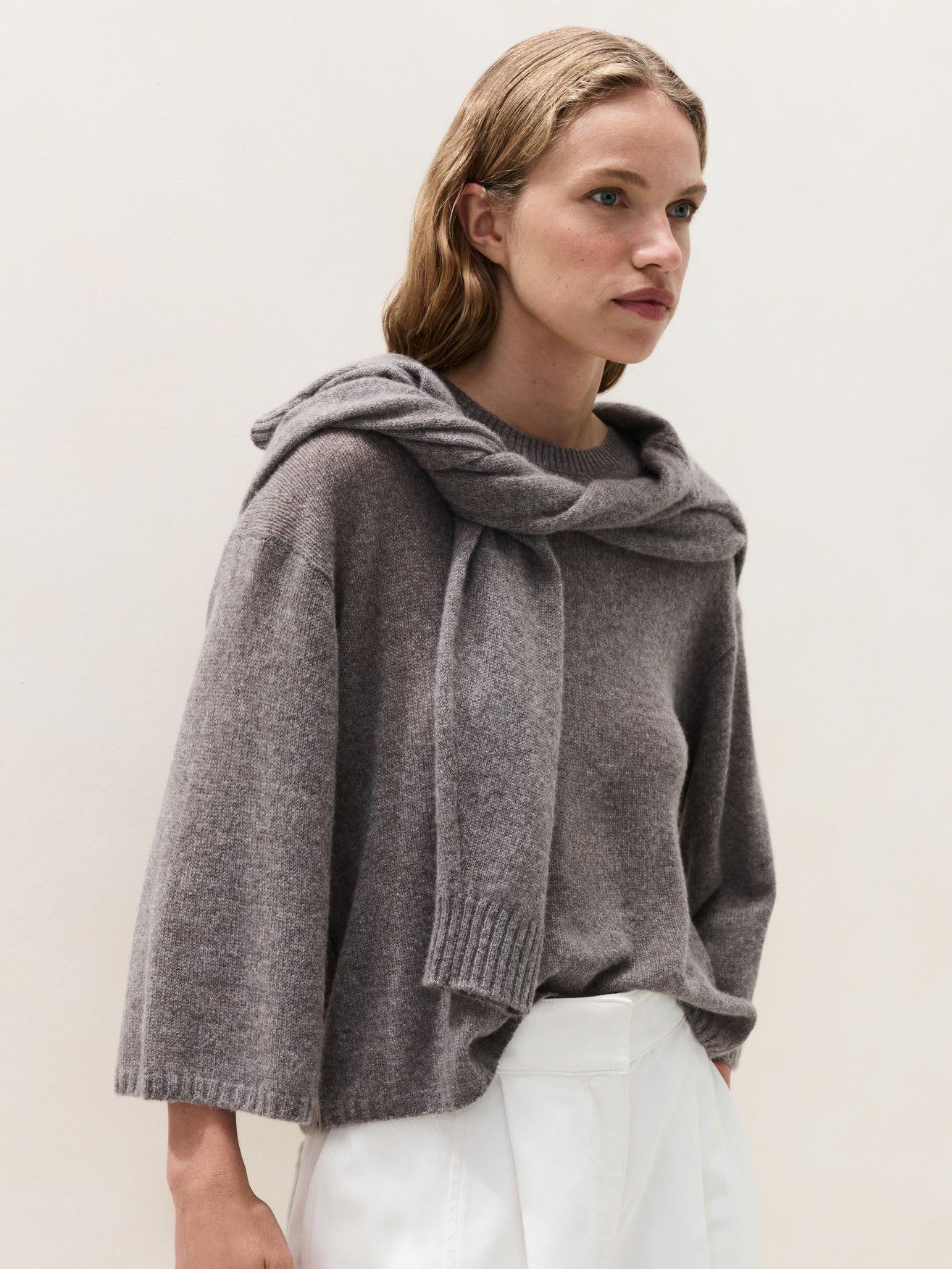 a woman in a grey sweater and white pants standing