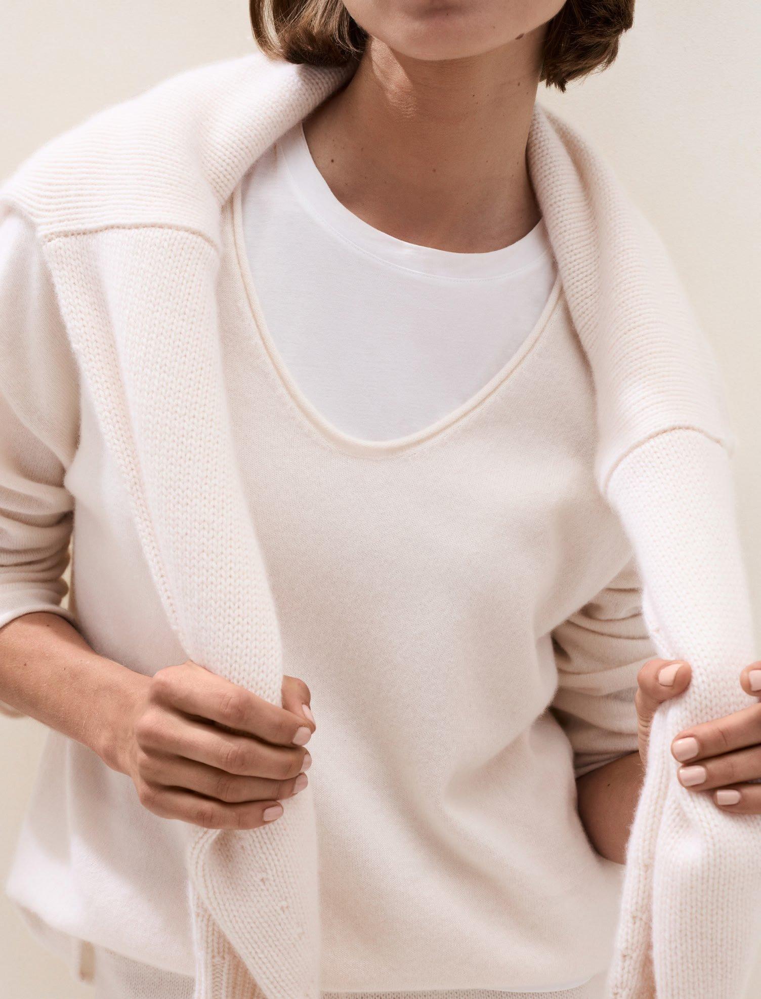 a woman in a white sweater and white pants holding a scarf