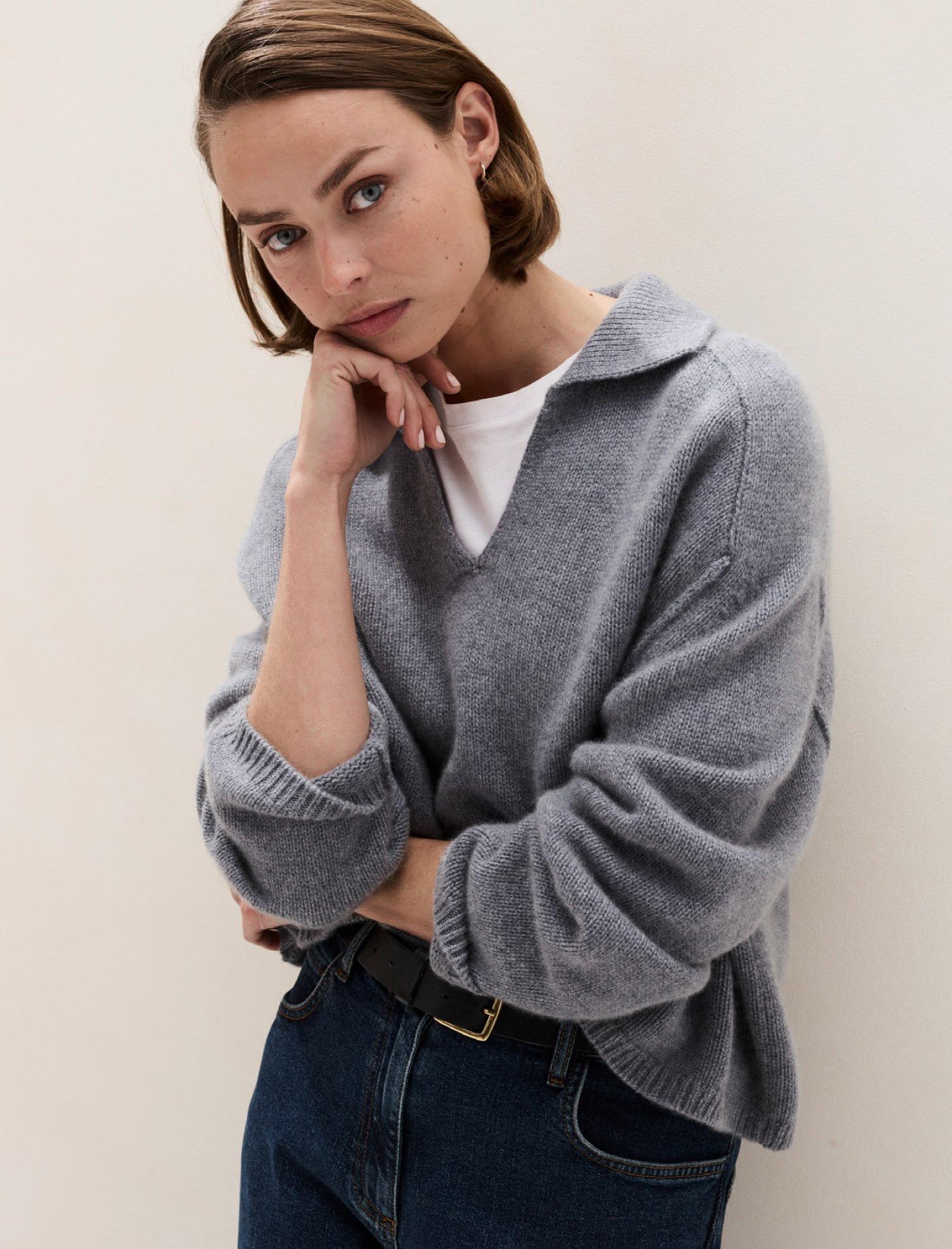 a woman in a grey sweater leaning against a wall