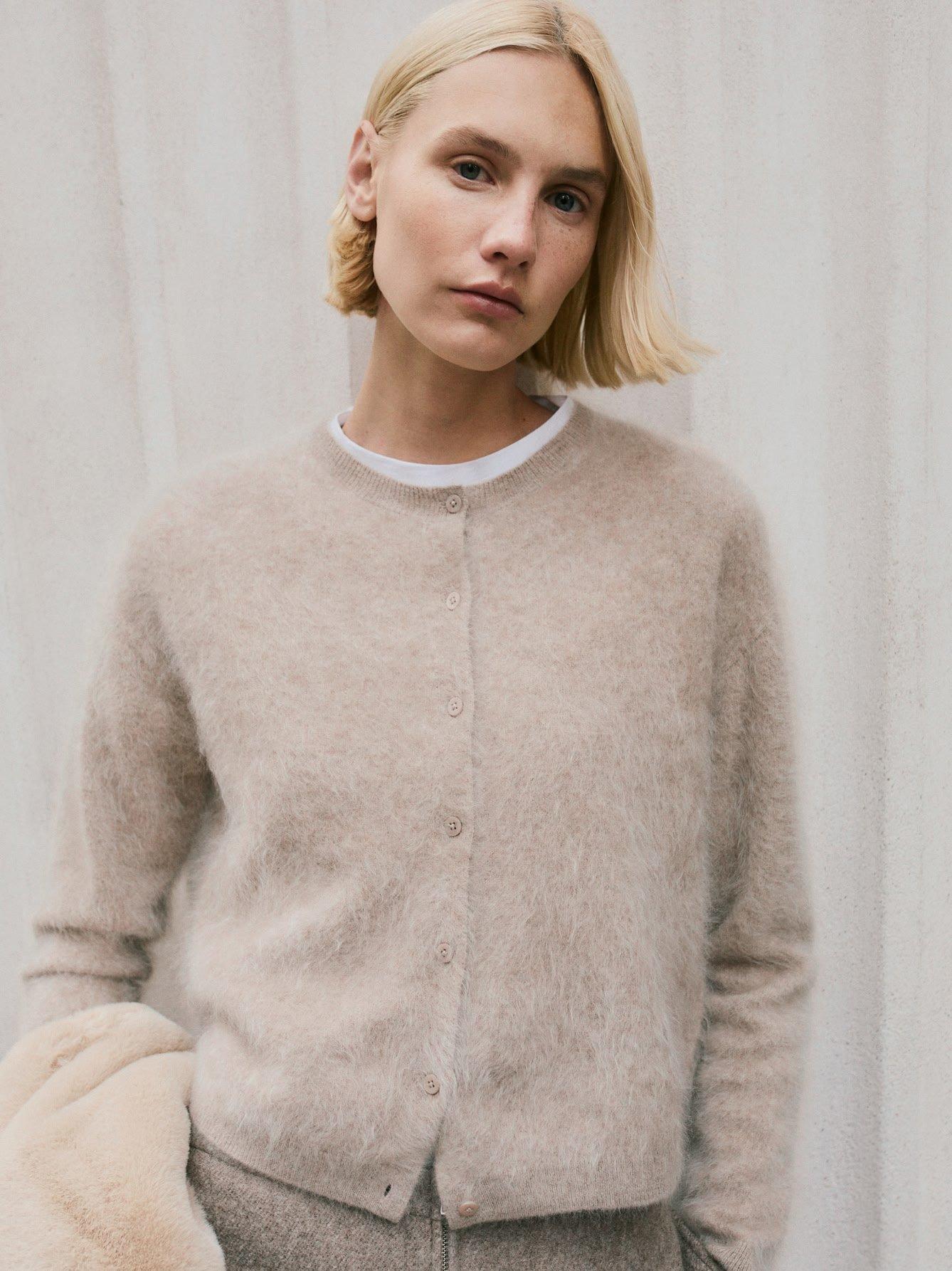 a woman in a beige cardigan and fur coat posing for a photo