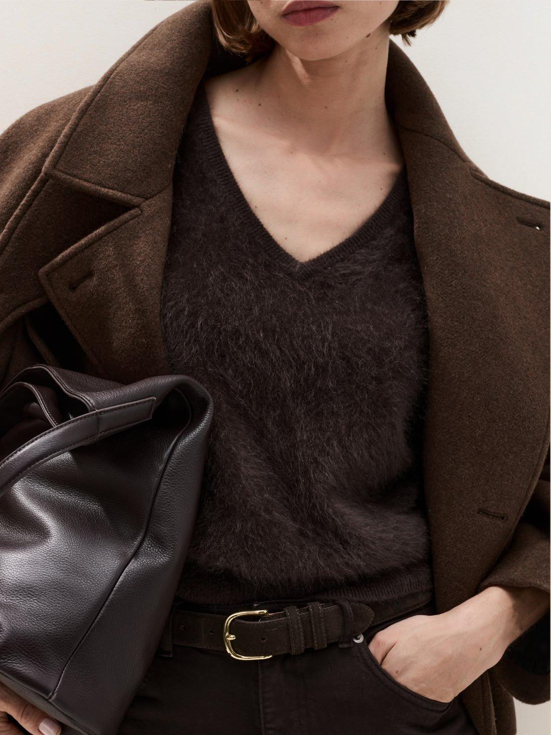 a woman in a brown coat holding a black purse