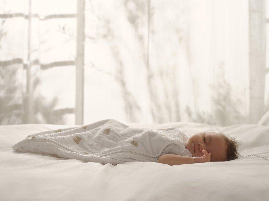 a baby sleeping on a bed with white sheets and curtains