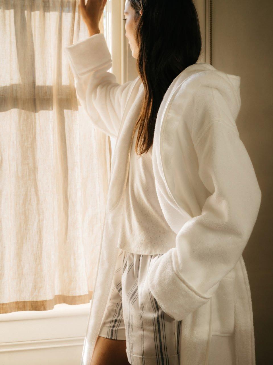 a woman in a white robe looking out a window