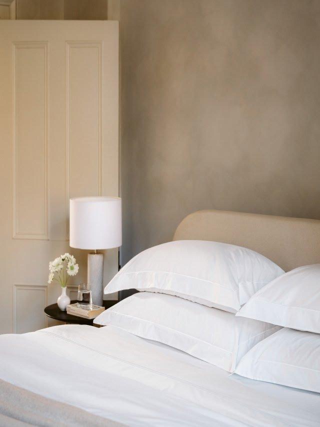 a bed with white sheets and pillows in a bedroom