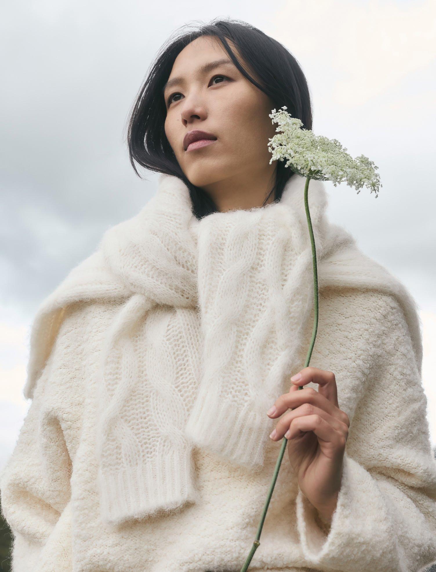 a woman in a white sweater holding a flower in her hand