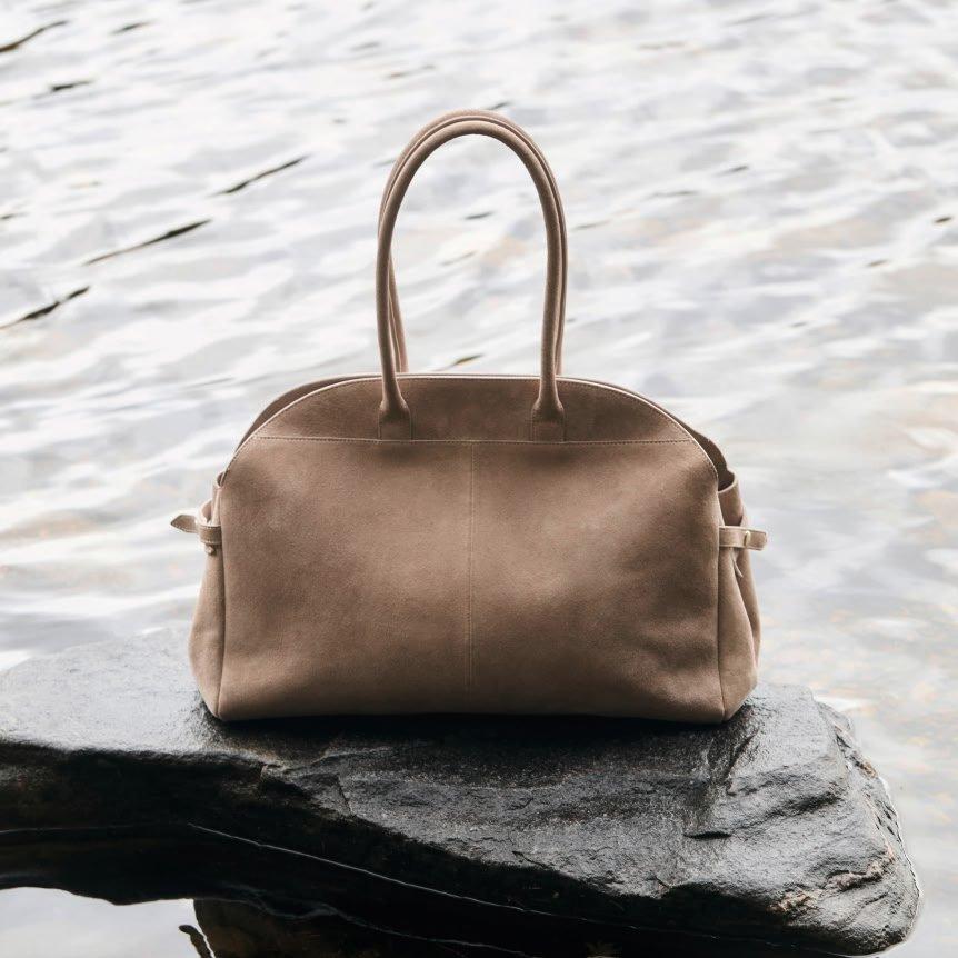a beige bag sitting on a rock in front of water