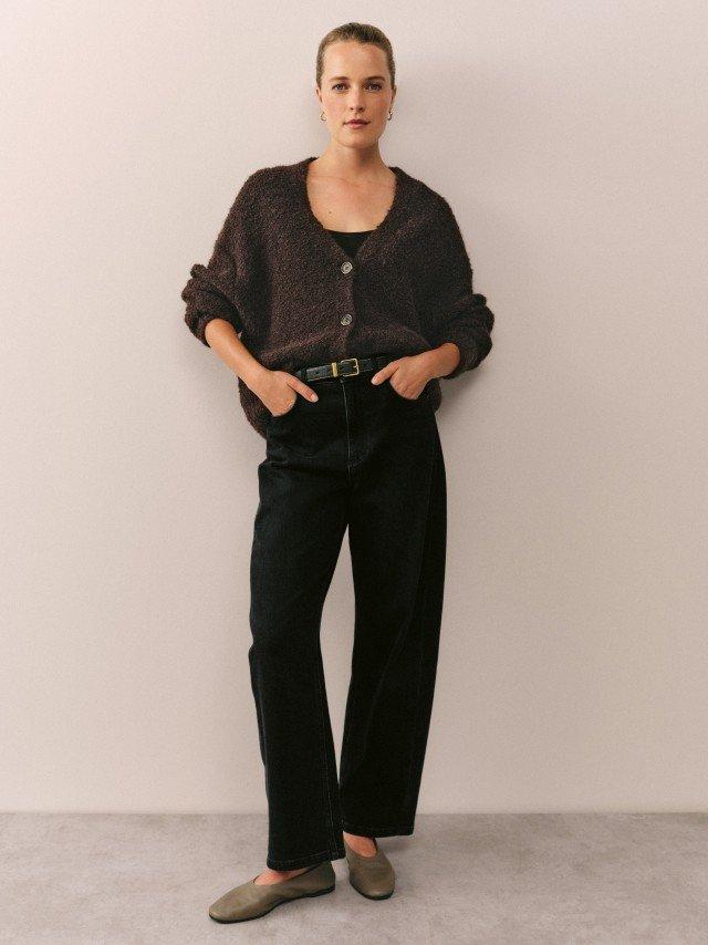 a woman in white pants and a beige jacket holding a black bag