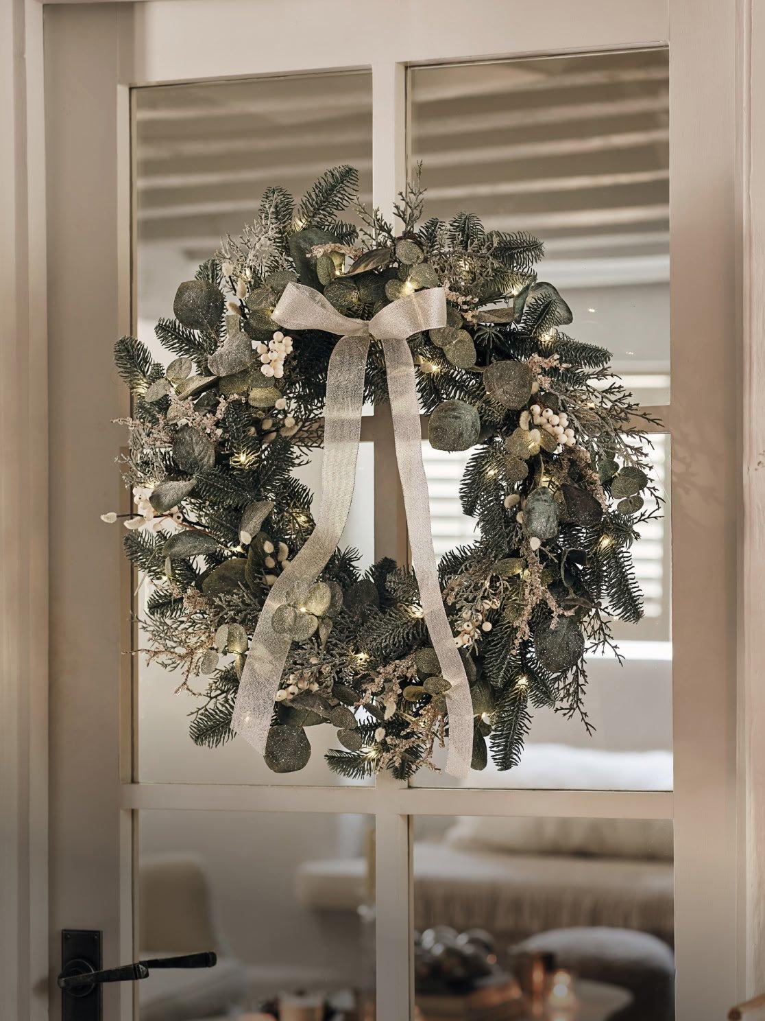 a wreath hanging from a door with a white bow