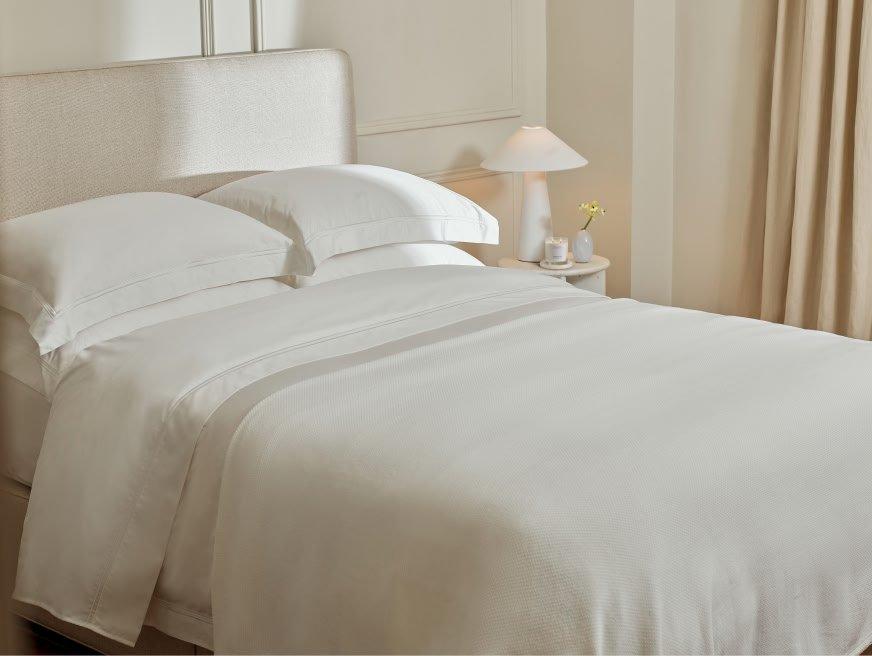 a bed with white sheets and pillows in a bedroom