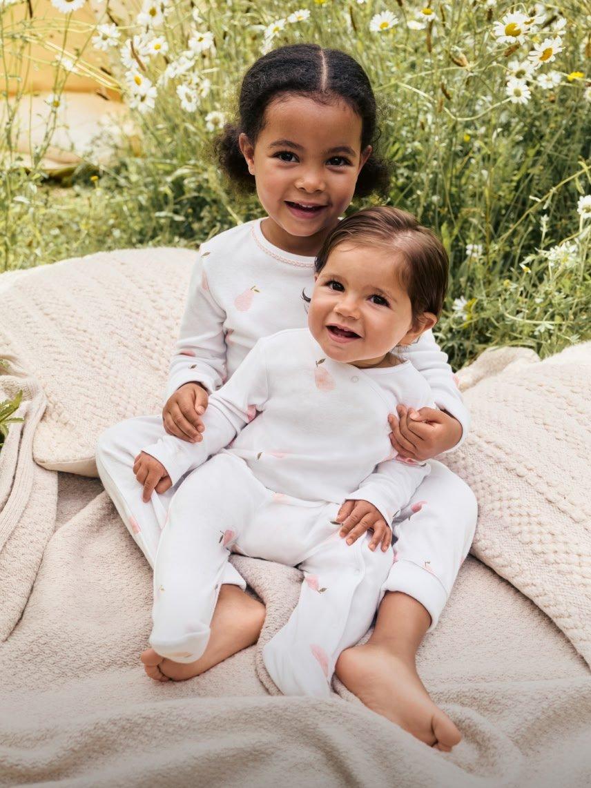 two children sitting on a blanket in front of a field
