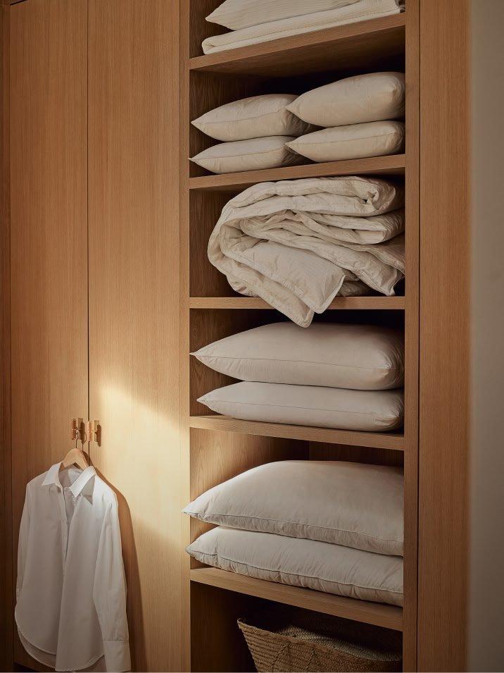 a closet with a white shirt hanging on a hanger and a stack of white pillows