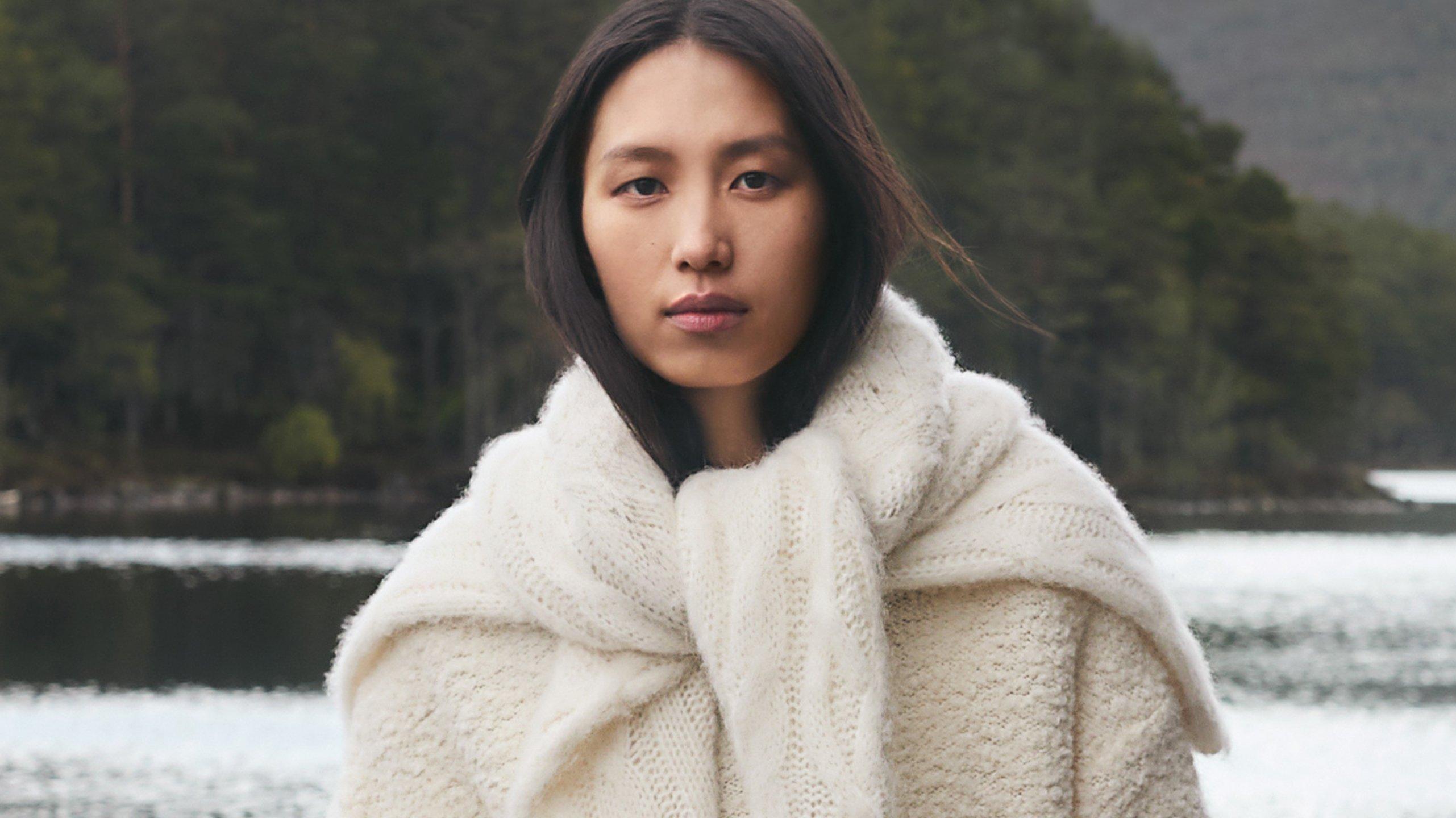 a woman in a white sweater standing in front of a lake