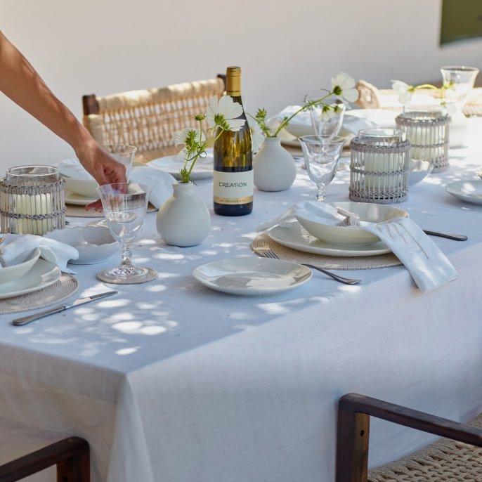 a table set with white table cloth and white plates and glasses